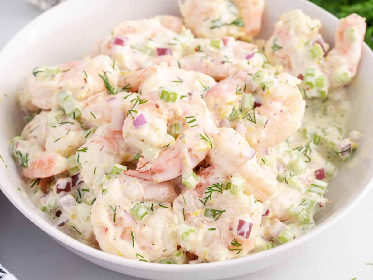A white bowl filled with creamy Shrimp Salad, featuring chopped celery, red onion, and fresh dill mixed with a mayonnaise-based dressing.