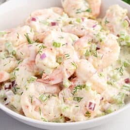 A white bowl filled with creamy Shrimp Salad, featuring chopped celery, red onion, and fresh dill mixed with a mayonnaise-based dressing.