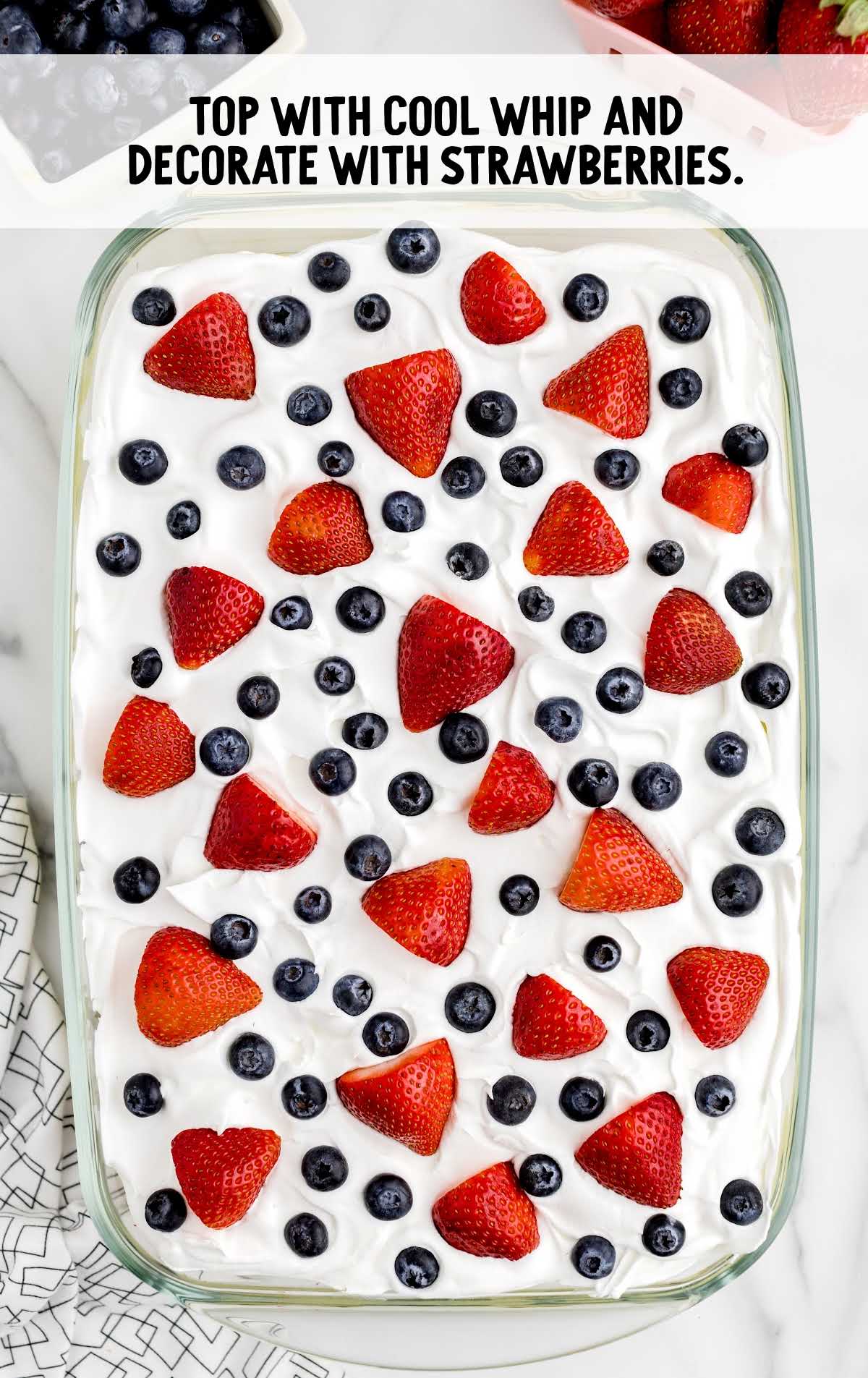 cake topped with cool whip and decorated with strawberries in a baking dish