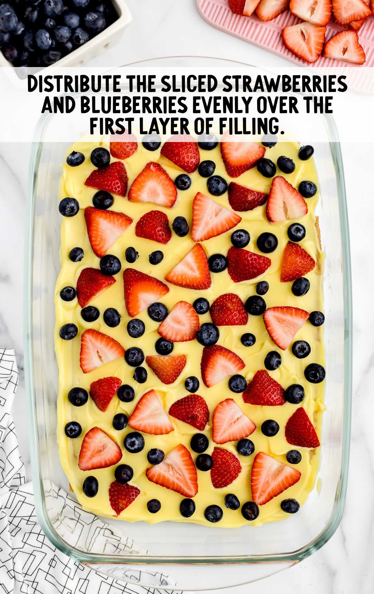 strawberries and blueberries distributed over the first layer of filling in a baking dish