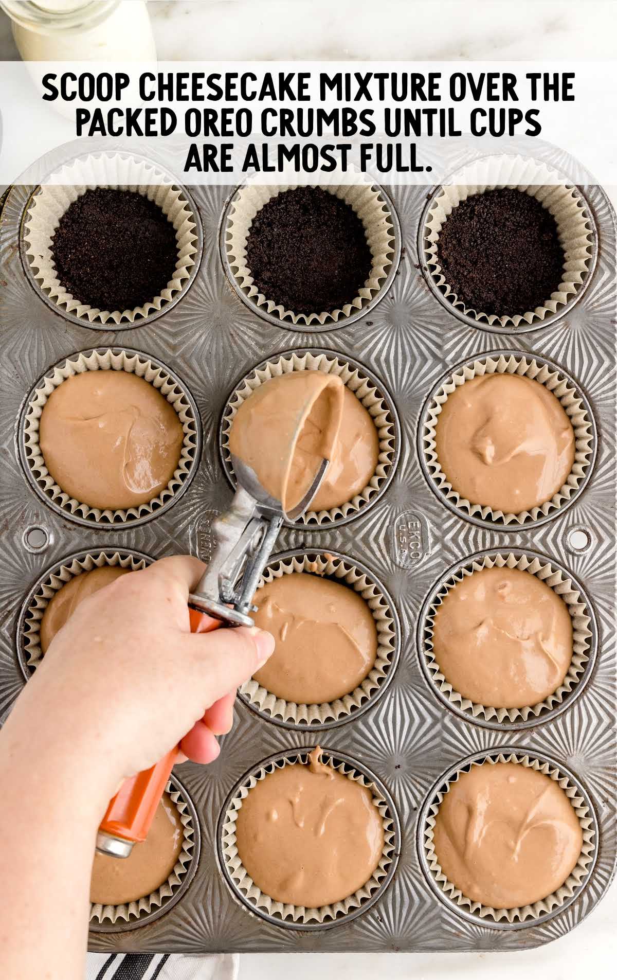 cheesecake mixture scooped over the oreo crumbs in a cupcake baking tray