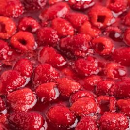 close up shot of raspberry pie on a plate topped with raspberries