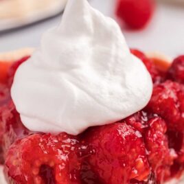 close up shot of a slice of raspberry pie topped with whipped cream
