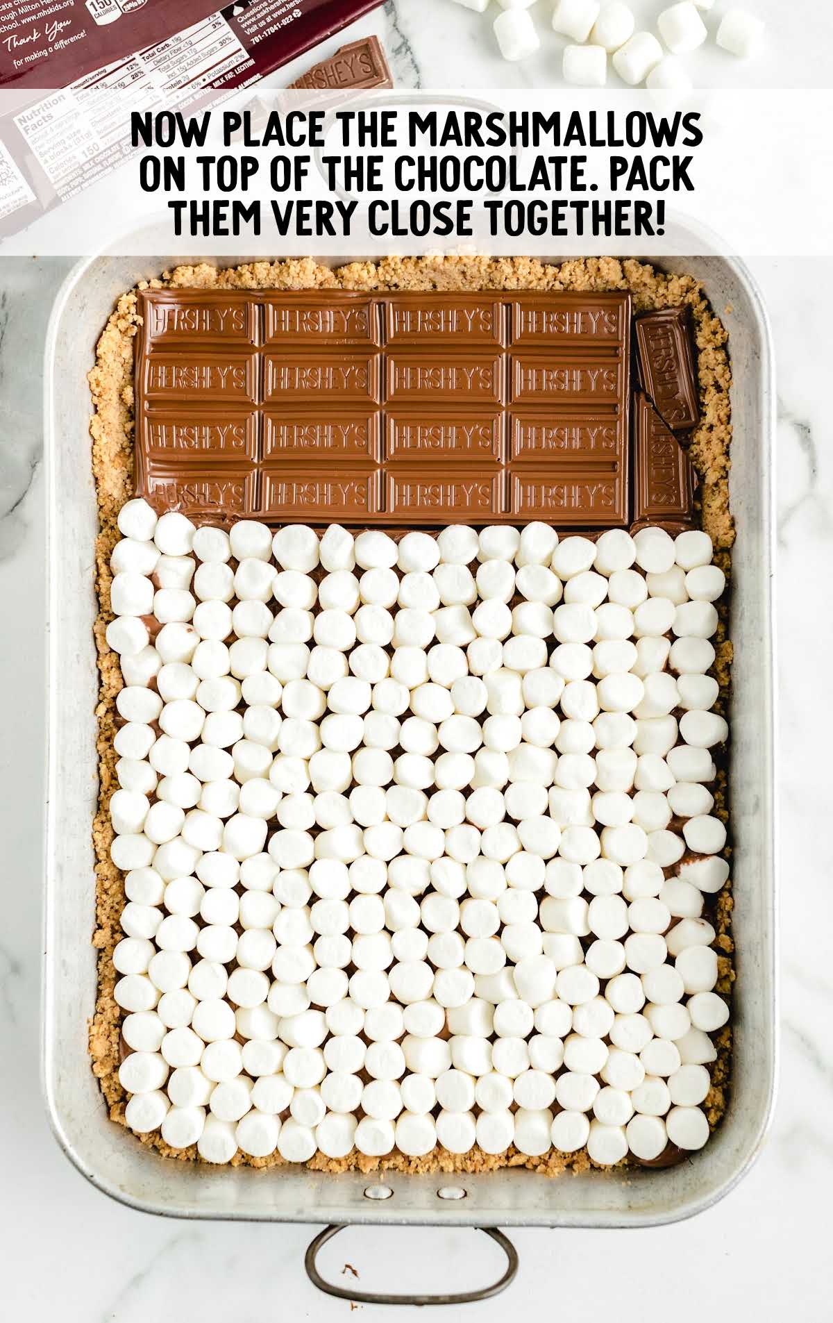 marshmallows placed on top of the chocolate in a baking dish