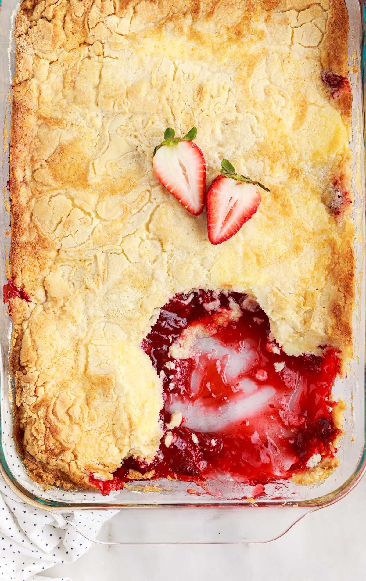 an overhead shot of Strawberry Cheesecake Dump Cake in a baking dish with a sliced strawberry and a slice taken out