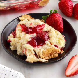 close up shot of a piece of Strawberry Cheesecake Dump Cake on a plate with a strawberry