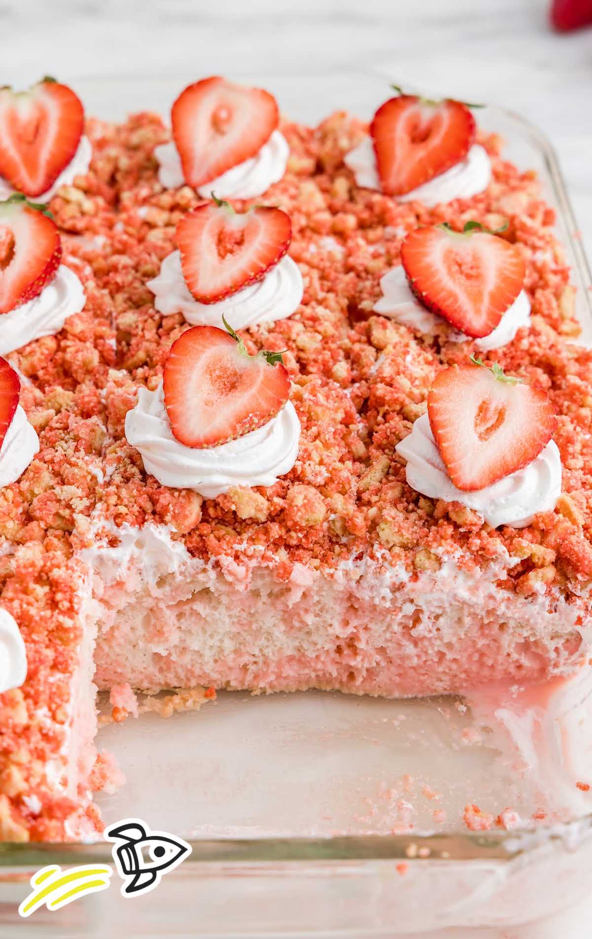 close up shot of Strawberry Crunch Poke Cake topped with whipped cream and a strawberries in a baking dish with slices taken out