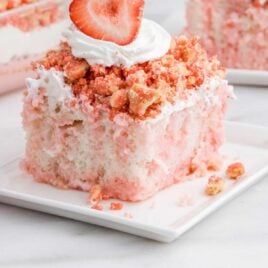 a slice of Strawberry Crunch Poke Cake topped with whipped cream and a strawberry on a plate