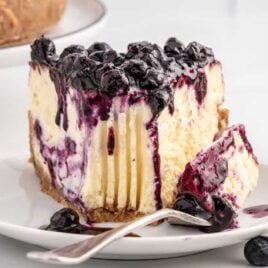 close up shot of a slice of Raspberry Pie on a plate topped with blueberries and a fork