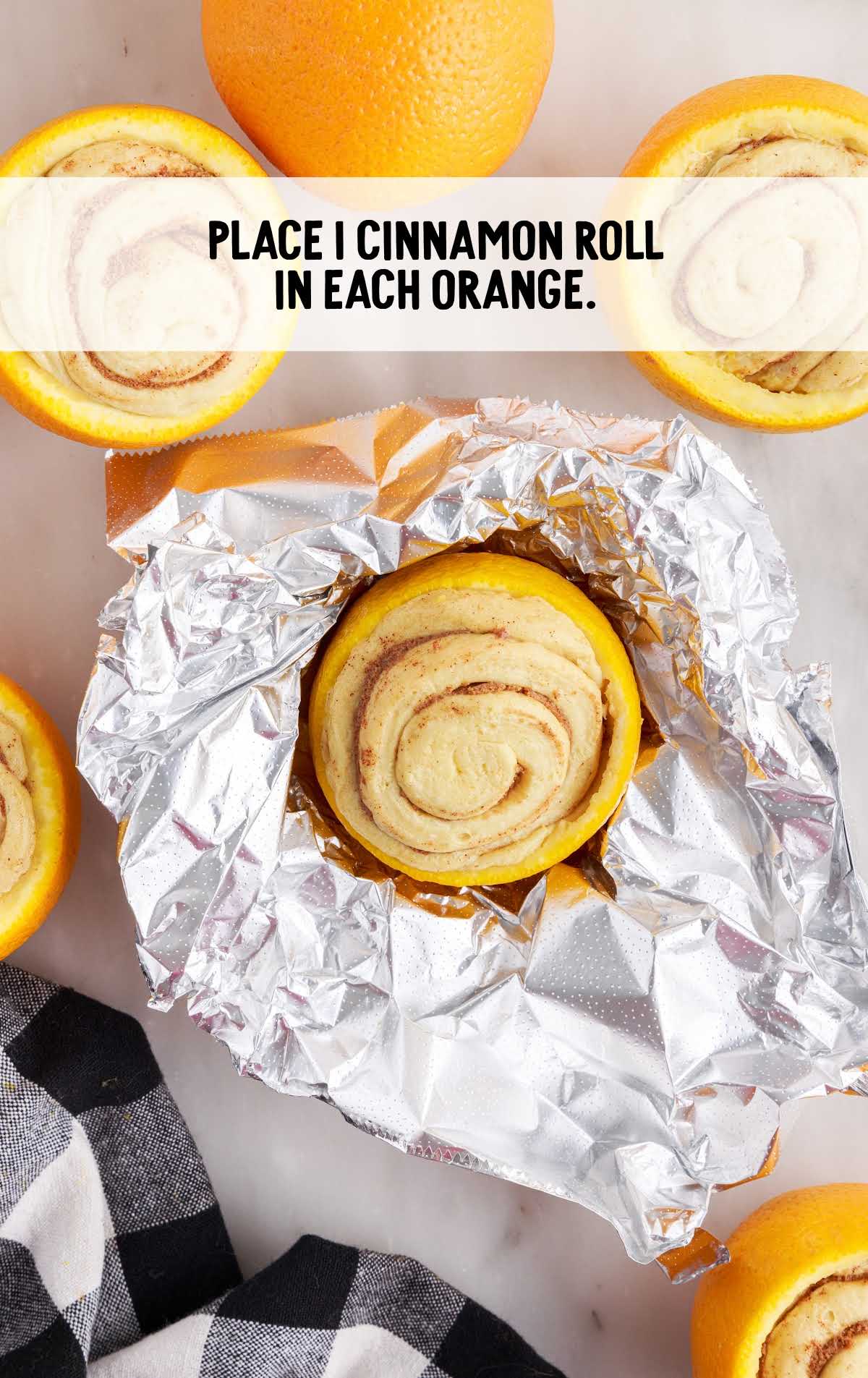 cinnamon roll placed in each orange on aluminum foil