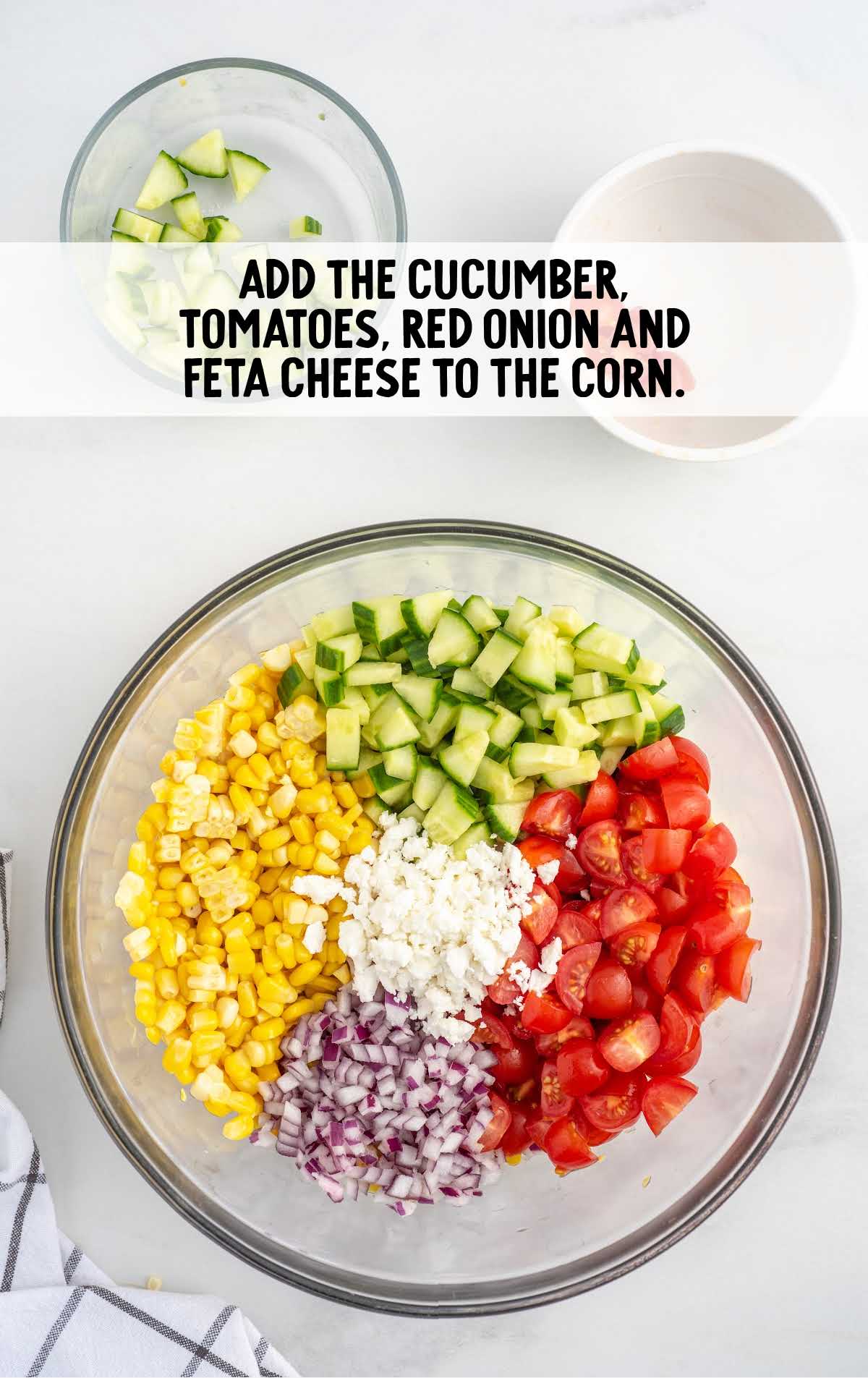 cucumber, tomatoes, red onion and feta cheese added to the corn in a bowl