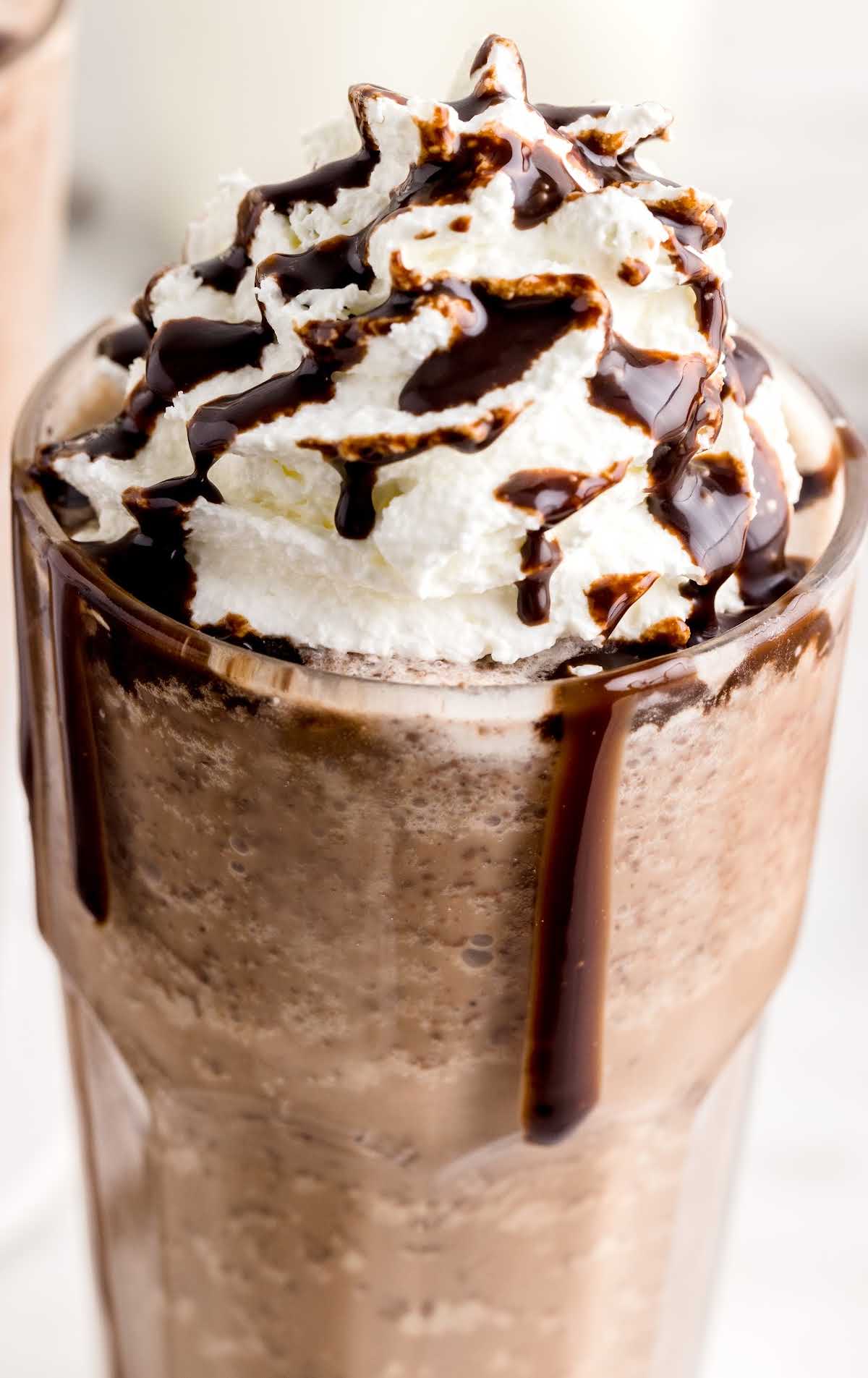 a close up shot of a Frappuccino topped with whipped cream, chocolate syrup, and chocolate chips in a tall glass