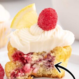 close up shot of Lemon Raspberry Cupcakes with a bite taken out of it topped with a raspberry and a slice of lemon
