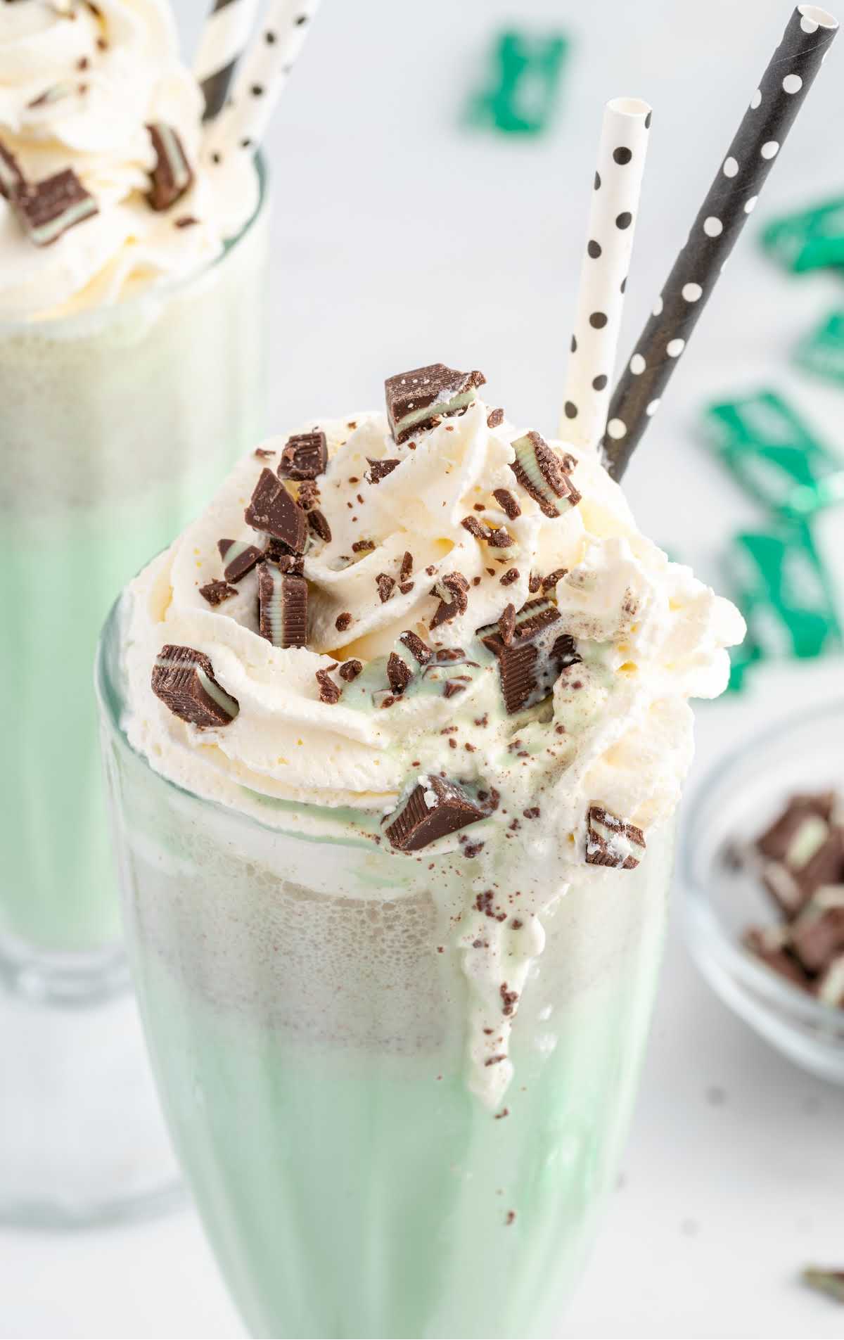 close up shot of Mint Chocolate Chip Milkshake in a tall glass topped with whipped cream and pieces of mint