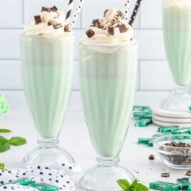 close up shot of Mint Chocolate Chip Milkshake in a tall glass topped with whipped cream and pieces of mint