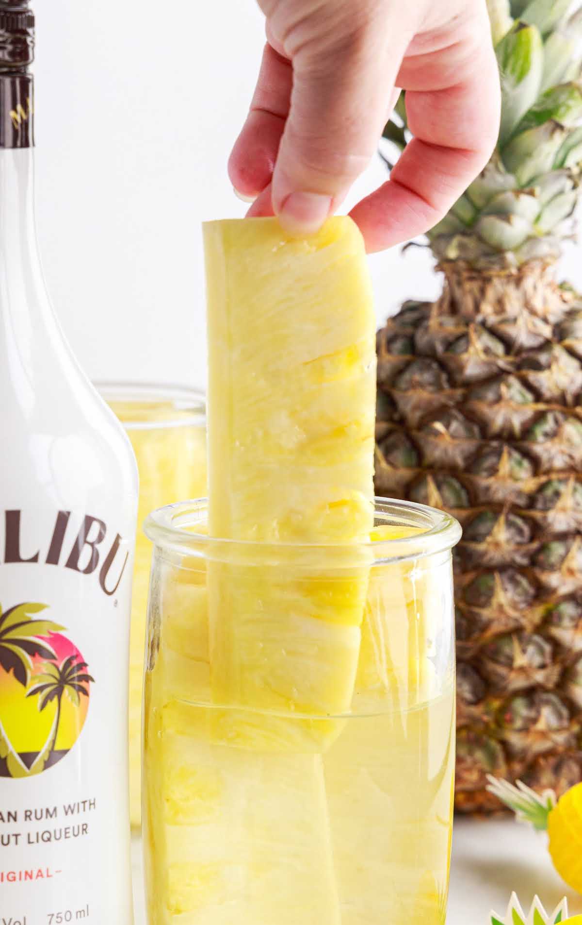 a close up shot of a tall container Pineapple Spears in Malibu Rum with a piece of pineapple taken out