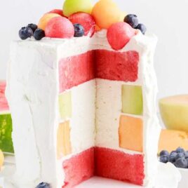 Watermelon Cake on a cake stand with a slice taken out topped melon balls and blueberries