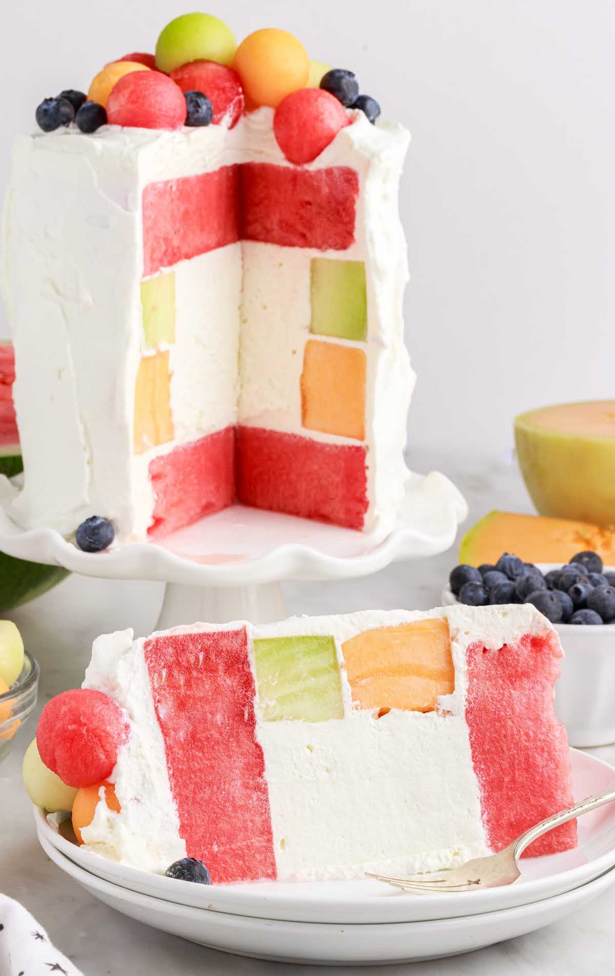 Watermelon Cake on a cake stand with a slice taken out and put on a plate