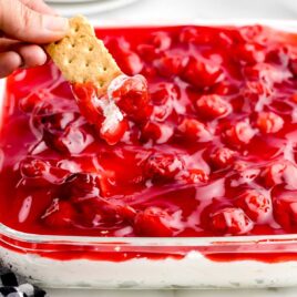 close up shot of graham cracker dipped into Cherry Cheesecake Dip in a baking dish