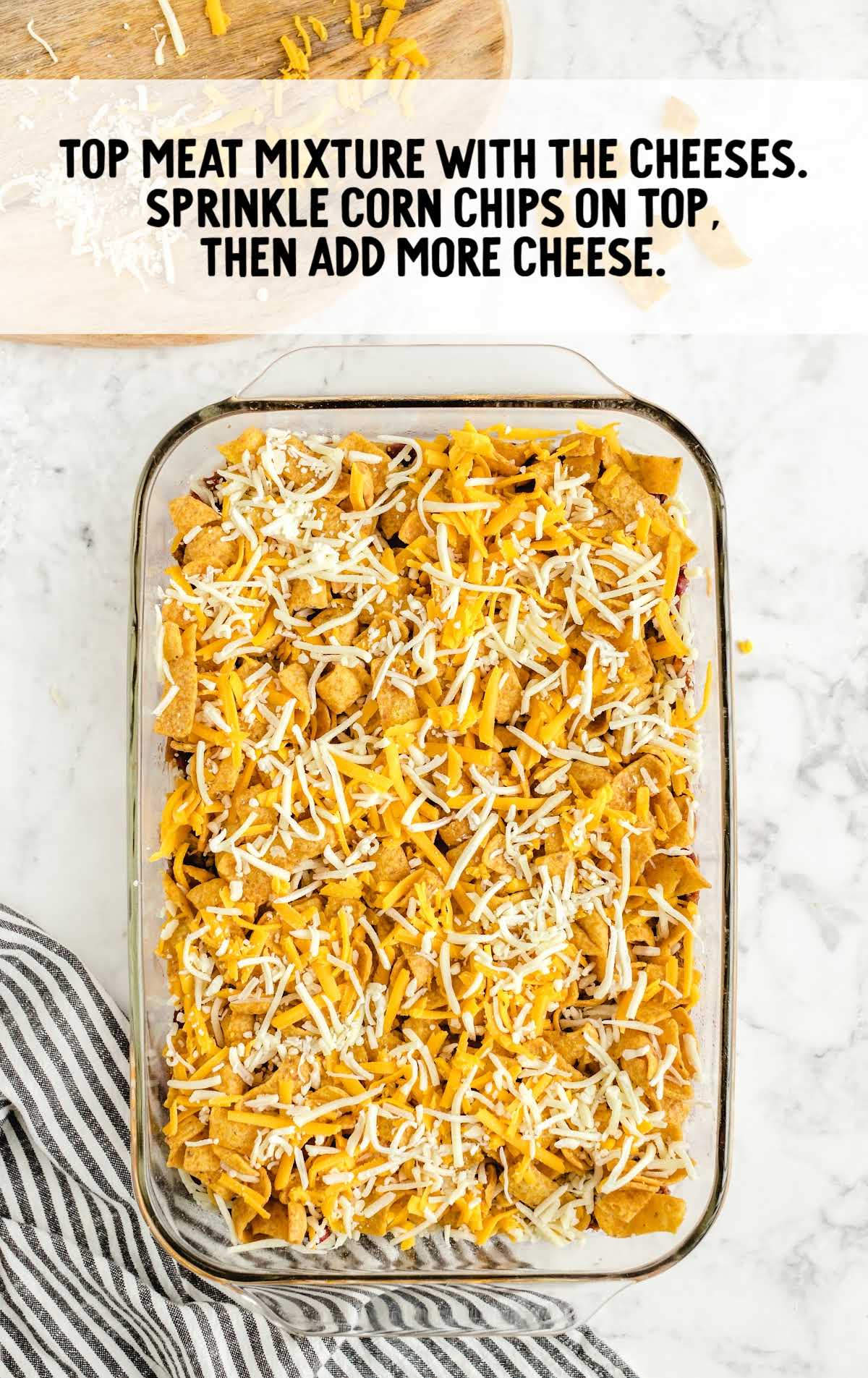 cheese and corn chips sprinkled on top of the mixture in a baking dish