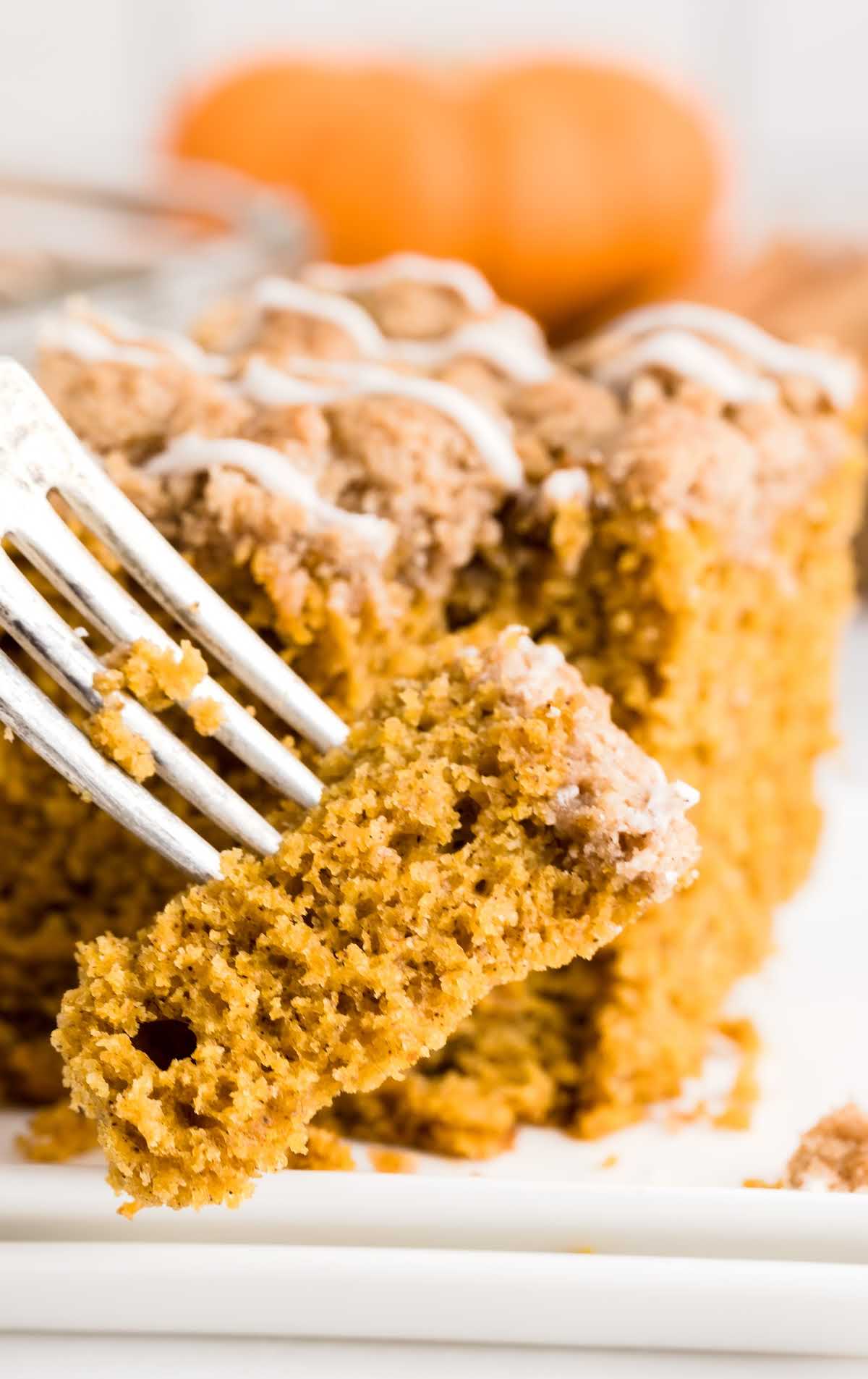 a close up shot of a slice of Pumpkin Coffee Cake on a plate with a fork grabbing a piece