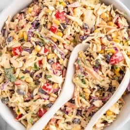 Top-down view of a bowl of Mexican coleslaw on a marble surface, with lime wedges and forks on the side.