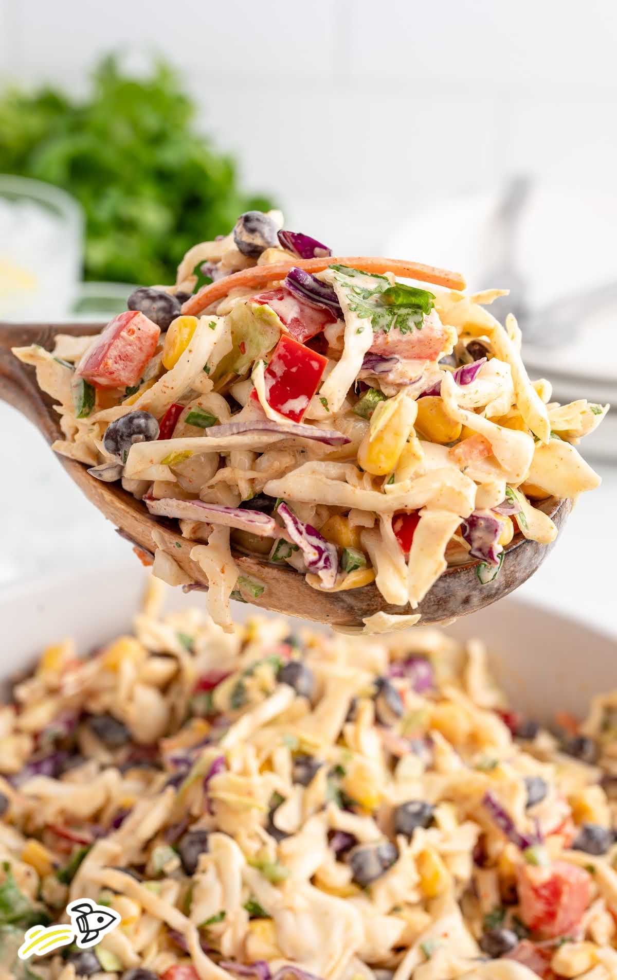 Wooden spoon lifting a serving of Mexican coleslaw over a bowl, highlighting the colorful veggies and dressing.