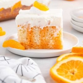 a close up shot of a slice of Orange Creamsicle Poke Cake on a plate topped with a mandarin