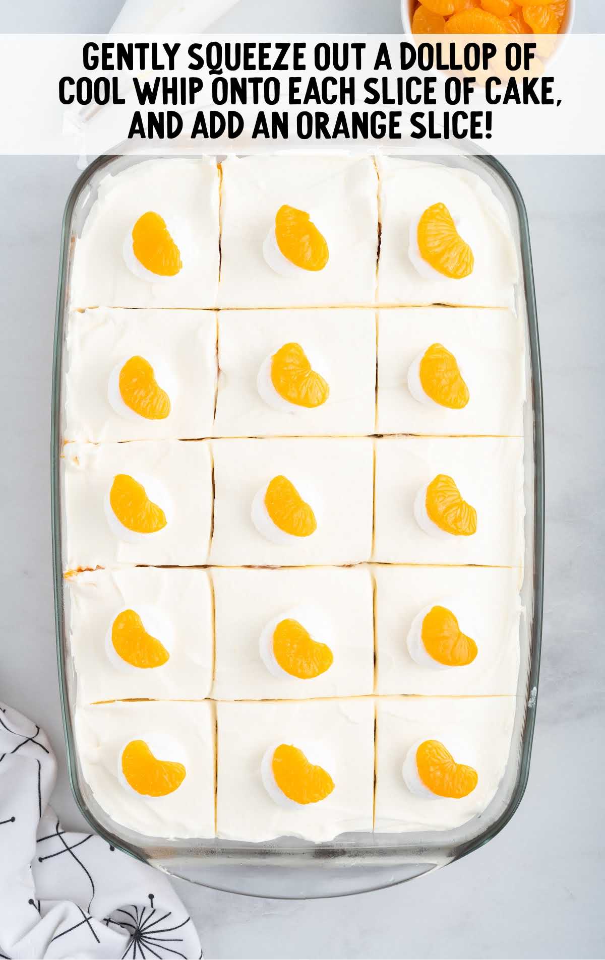 cool whip and orange slices added to the cake in a baking dish