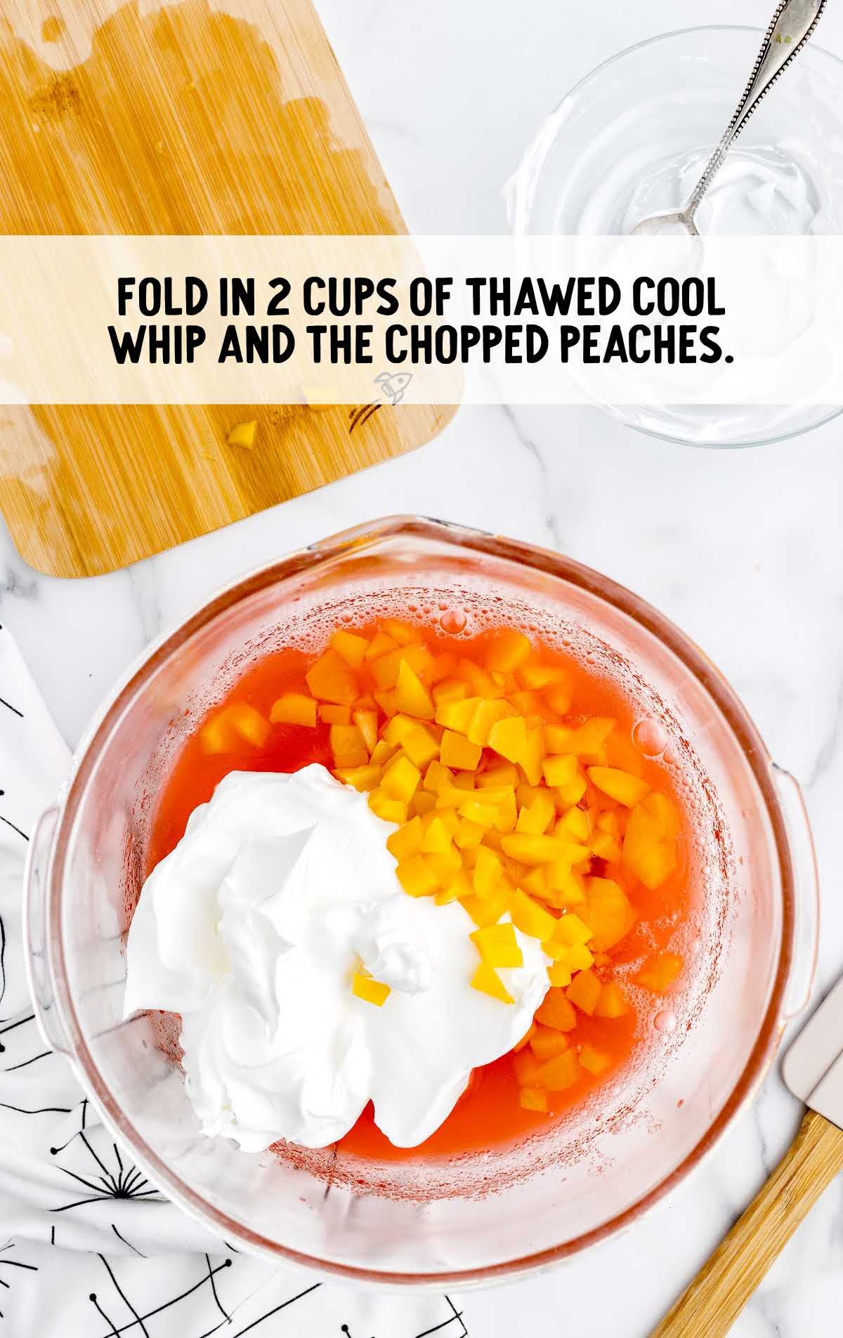 thawed cool whip and chopped peaches folded in a bowl