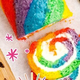 close up shot of Rainbow Roll Cake on a wooden board with a slices cut off