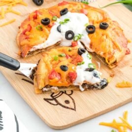 a close up shot of a spatula grabbing a piece of Taco Bell Mexican Pizza on a wooden board