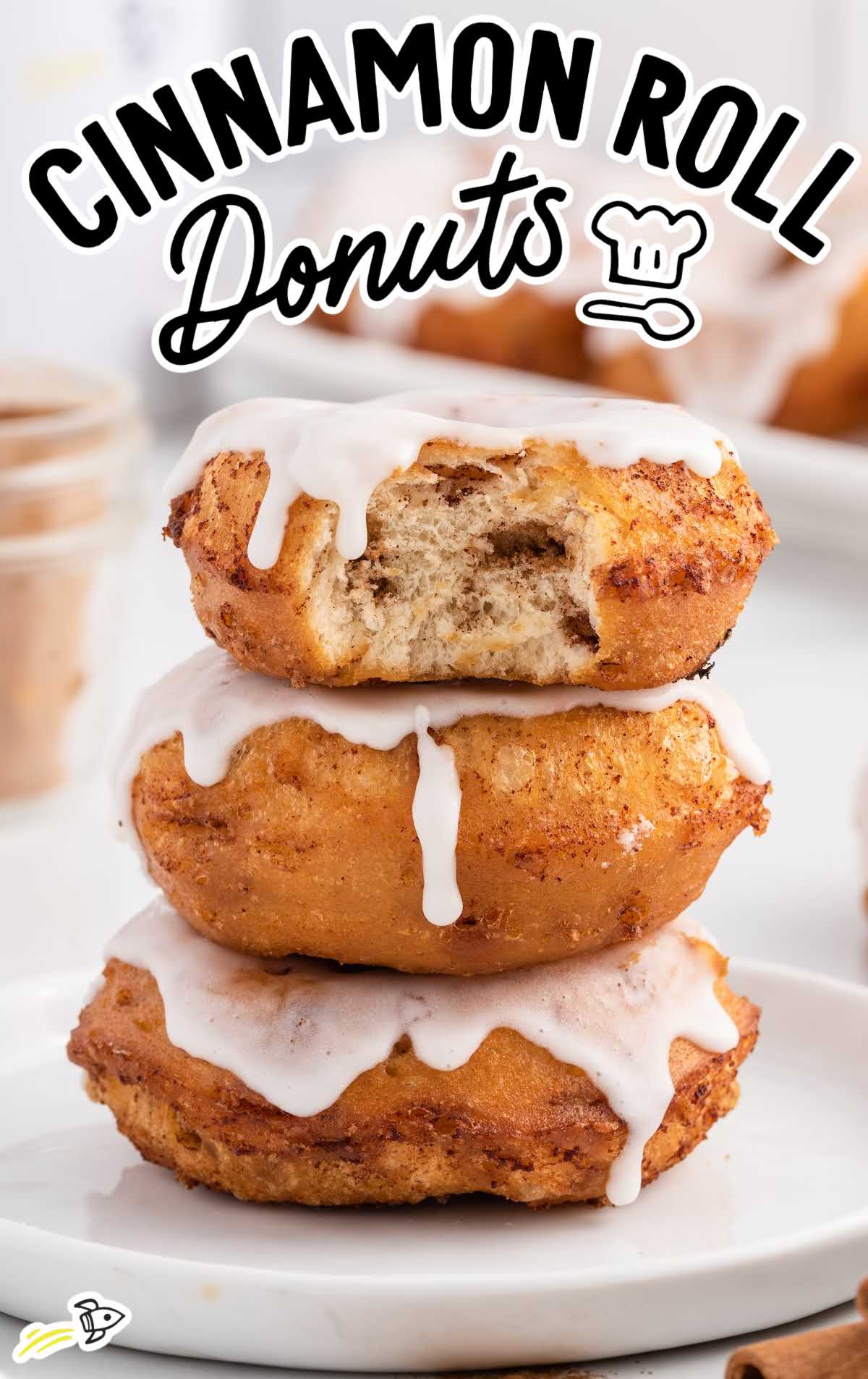 a close up shot of Cinnamon Roll Donuts stacked on top of each other with one having a bite taken out of it