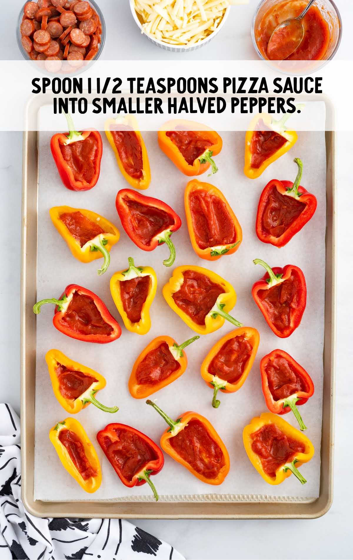 pizza sauce spooned into the halved peppers in a baking tray