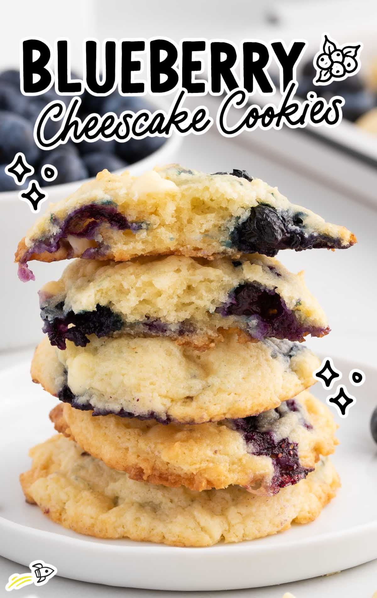close up shot of Blueberry Cheesecake Cookies stacked on top of each other with one cookie split in half on a plate