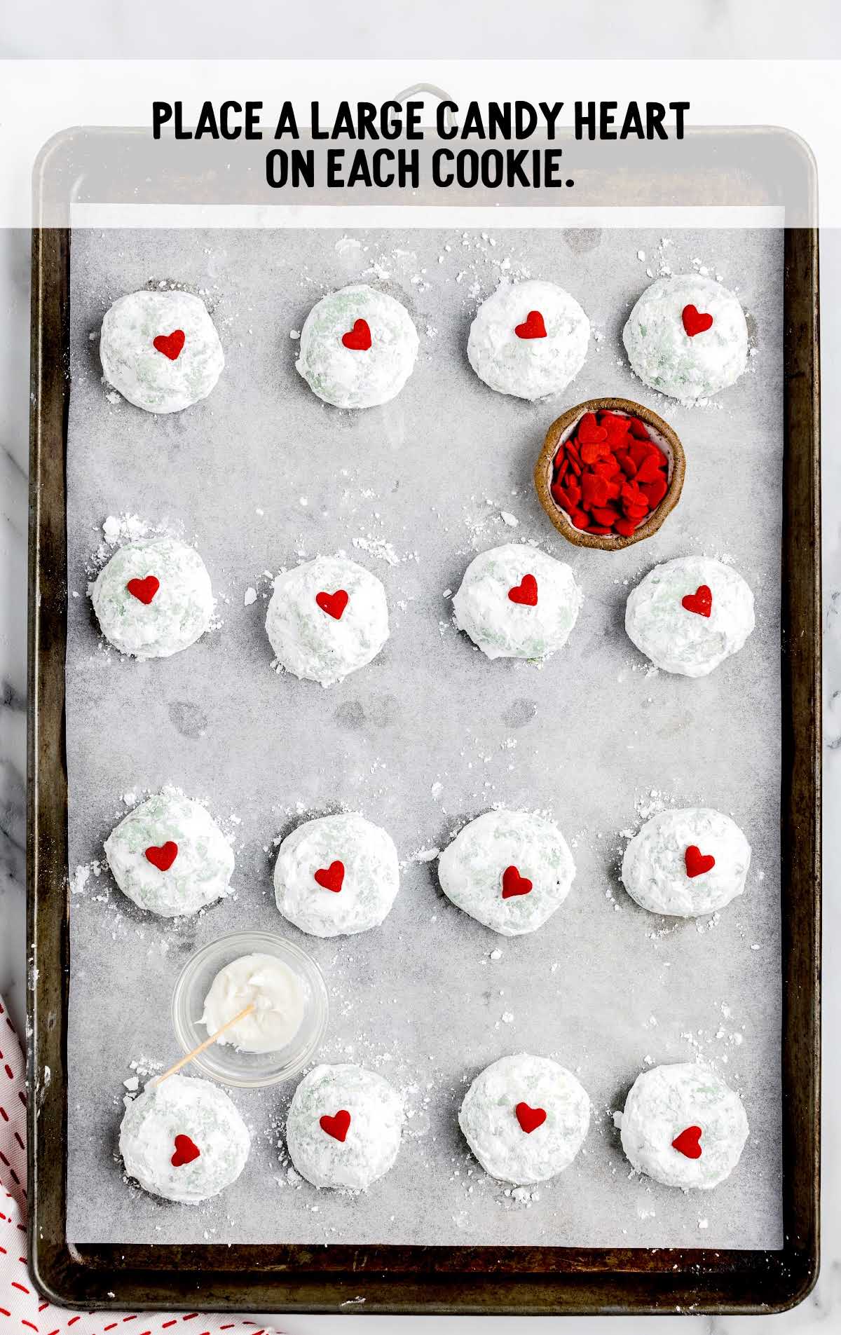 candy hearts placed on top of each snowball cookie on a baking sheet