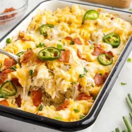 close up shot of Jalapeño Popper Chicken Pasta Casserole in a baking dish with a spoon grabbing a piece
