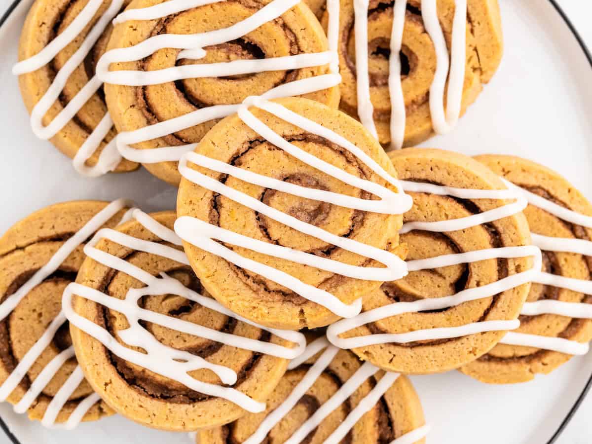 A close-up of several Pumpkin Roll Cookies topped with white icing, arranged on a white plate.