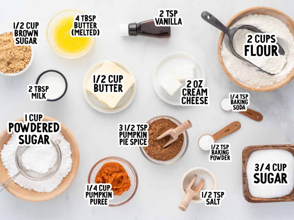 Baking ingredients arranged on a white surface, labeled with names and amounts, including flour, sugars, butter, cream cheese, milk, pumpkin, spices, and baking agents—perfectly prepared for making delicious Pumpkin Roll Cookies.