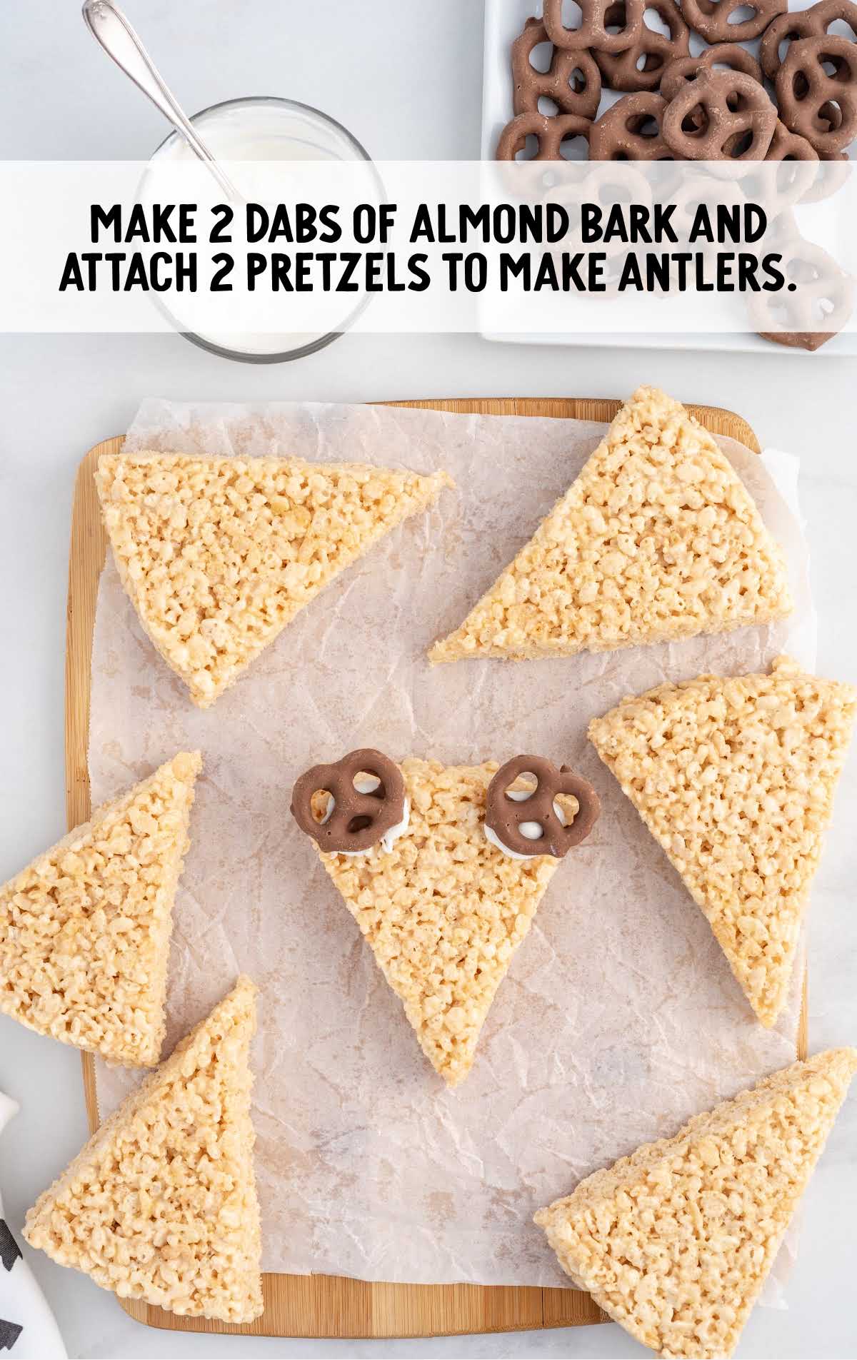 using almond bark attach pretzel to make antlers on a wooden board
