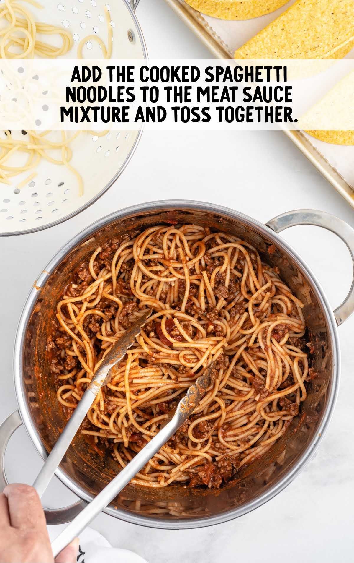 spaghetti noodles added to the meat sauce mixture in a pot