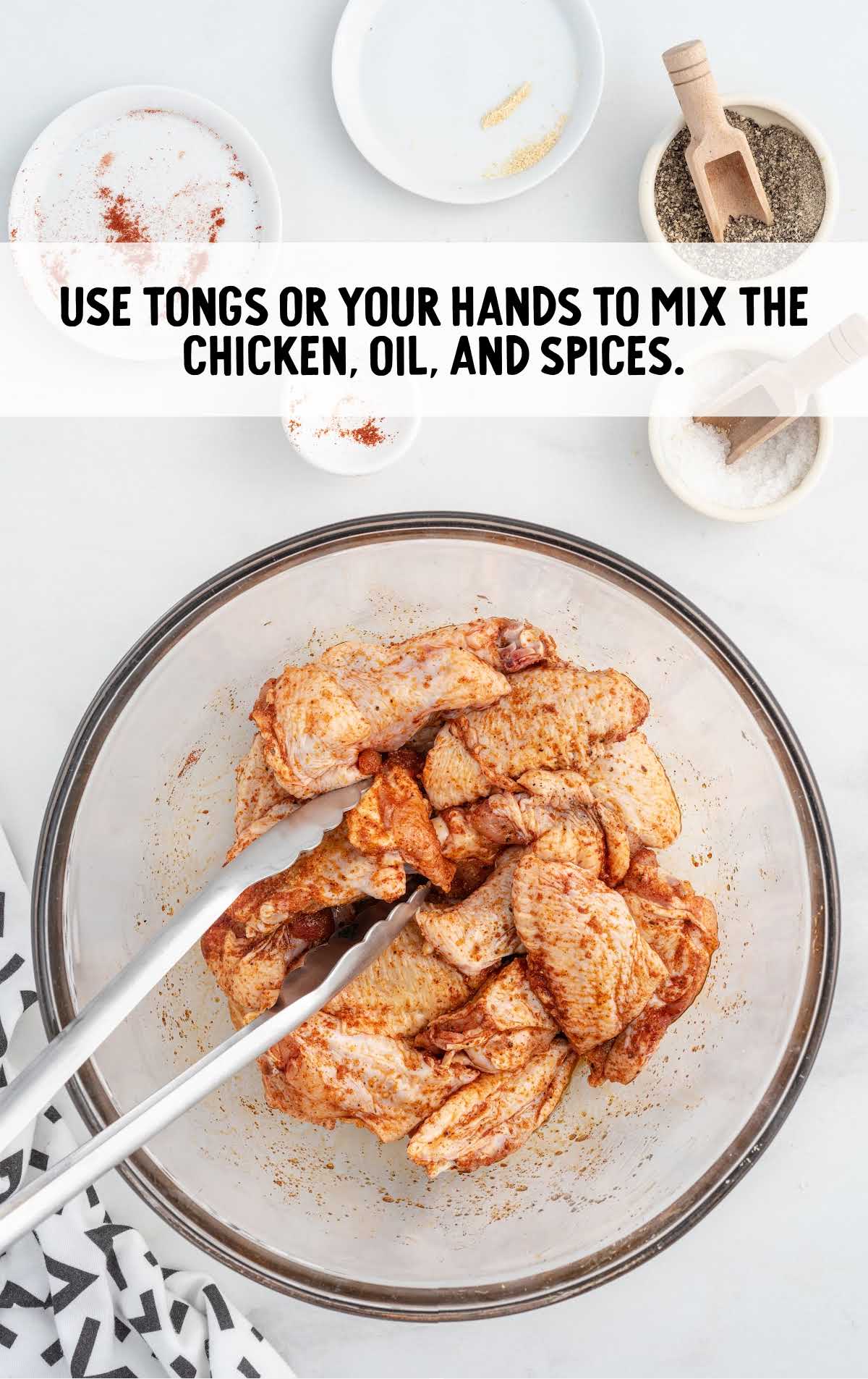 chicken, oil, and spices mixed in a bowl using hands or tongs