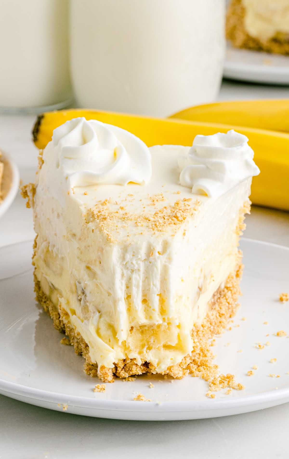 a close up shot of a slice of Banana Cream Cheesecake on a plate with a bite taken out of it