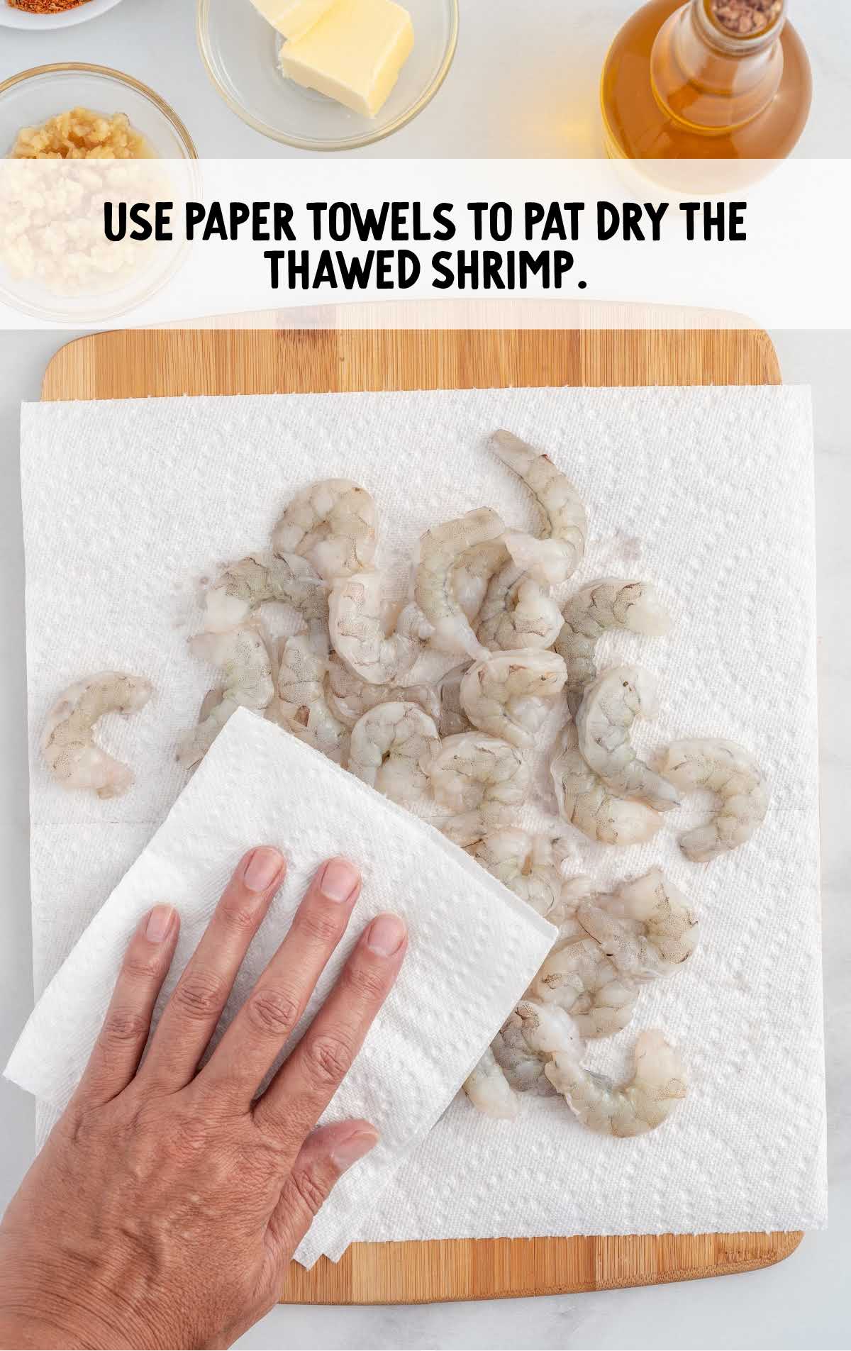 using paper towels pat dry the thawed shrimp on a wooden board