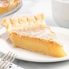 a close up shot of a slice of Chess Pie dusted with powdered sugar on a plate with a fork