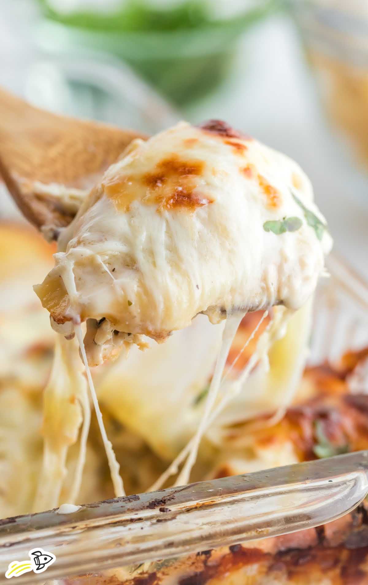 a close up shot of Chicken Stuffed Shells in a baking dish with a wooden spoon getting a slice