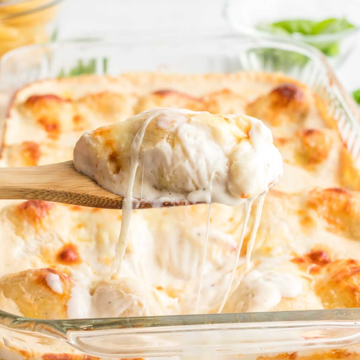 a close up shot of Chicken Stuffed Shells in a baking dish with a wooden spoon getting a slice