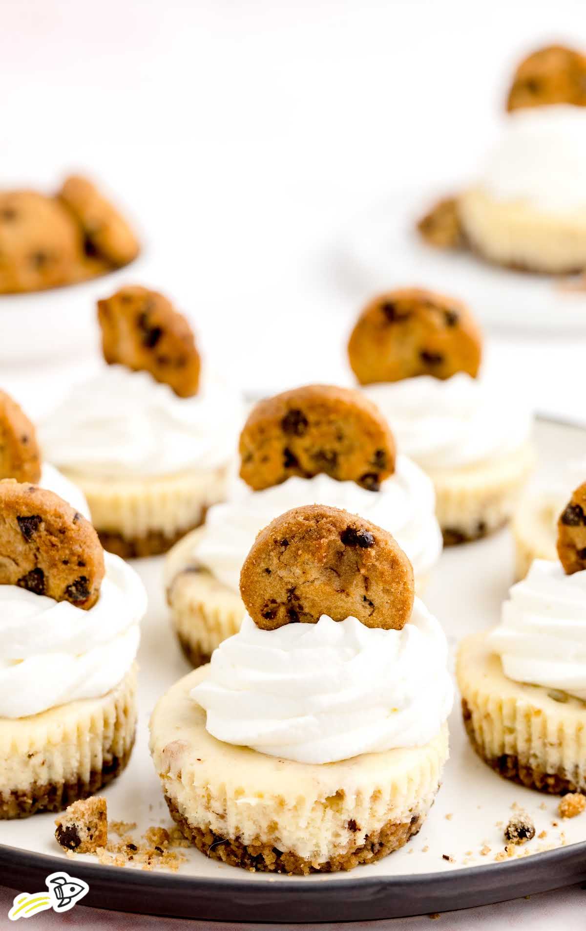 a close up shot of Chocolate Chip Cookie Cheesecakes with a bite taken out topped with a cookie on a platter