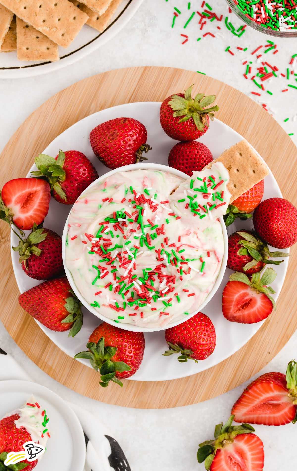 a close up shot of Christmas Sugar Cookie Dip in a bowl topped with a graham cracker with strawberries around it