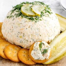 a close up shot of Dill Pickle Cheese Ball with crackers and a sliced pickle on a wooden board